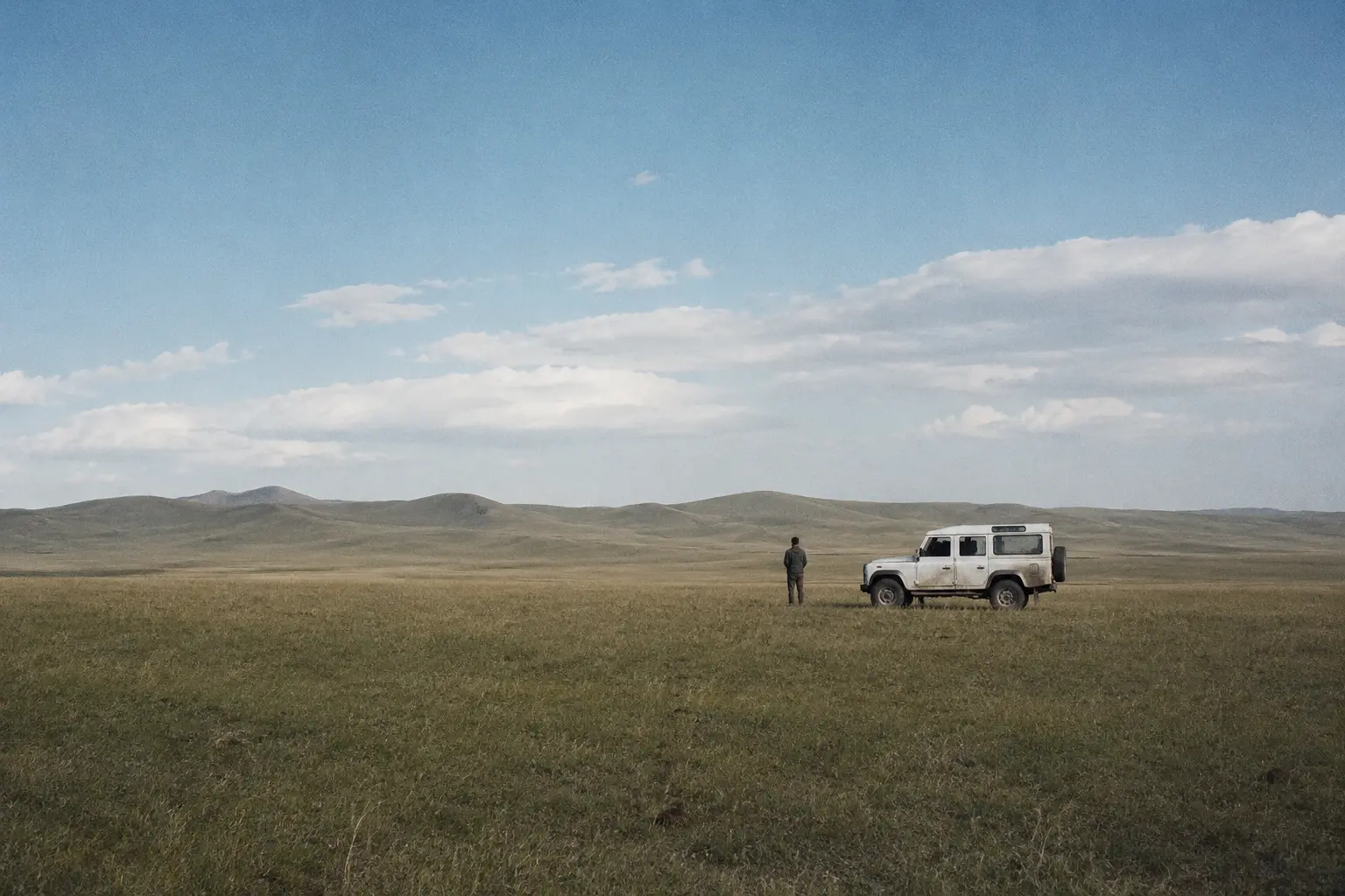 A figure and vehicle in a wide grassland